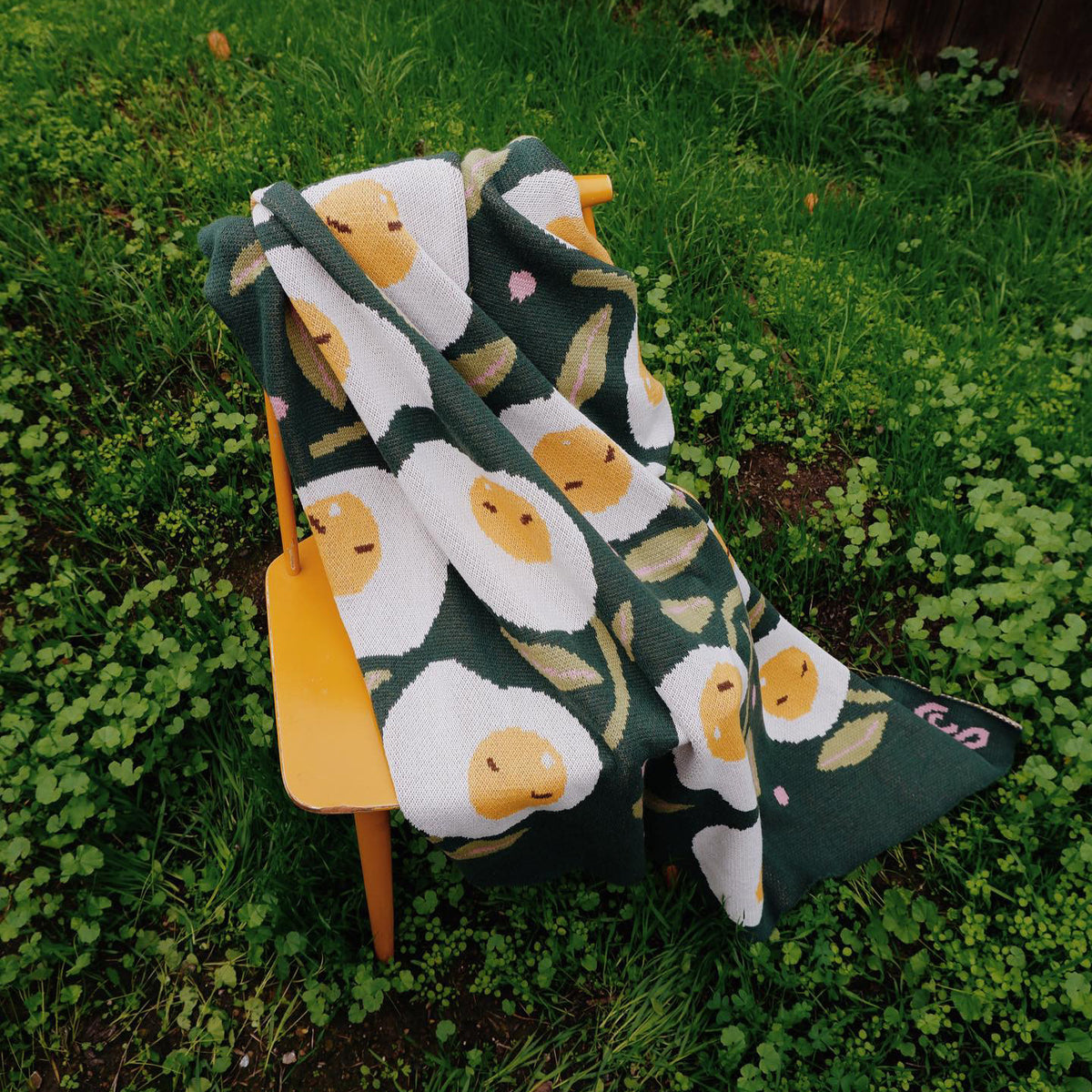 Green sunnyside blanket propped over a yellow chair on grass